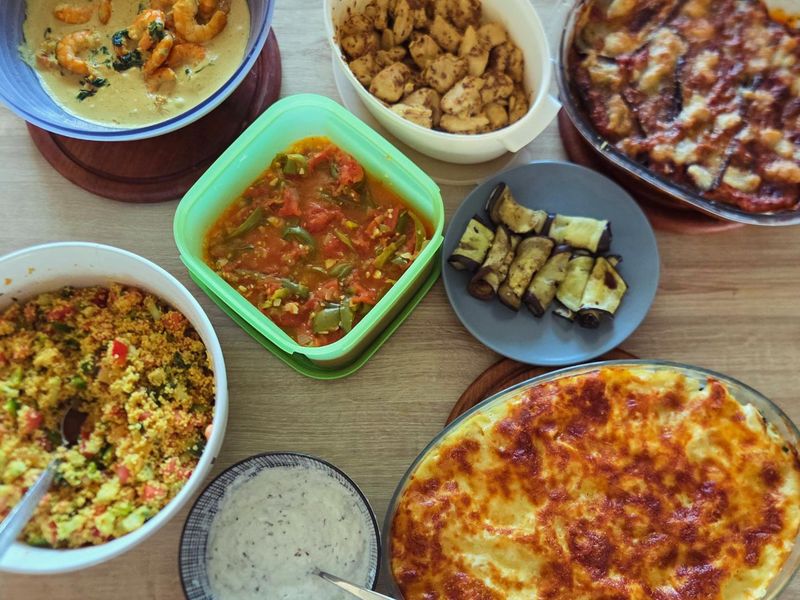 Plusieurs plats de la semaine disposés sur une table : gratin doré, taboulé, curry de crevettes, sauce au fromage blanc