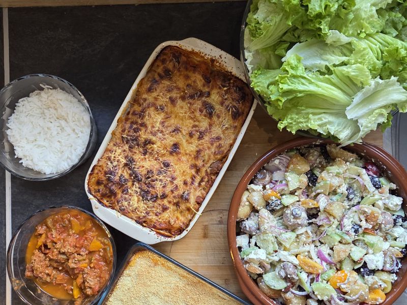 Plat de lasagnes gratinées entouré de riz, d'une salade de pommes de terre et de salade verte