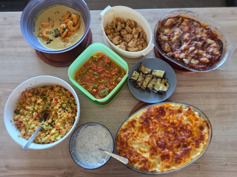 Plusieurs plats variés disposés sur une table en bois : gratin, taboulé, curry, aubergines